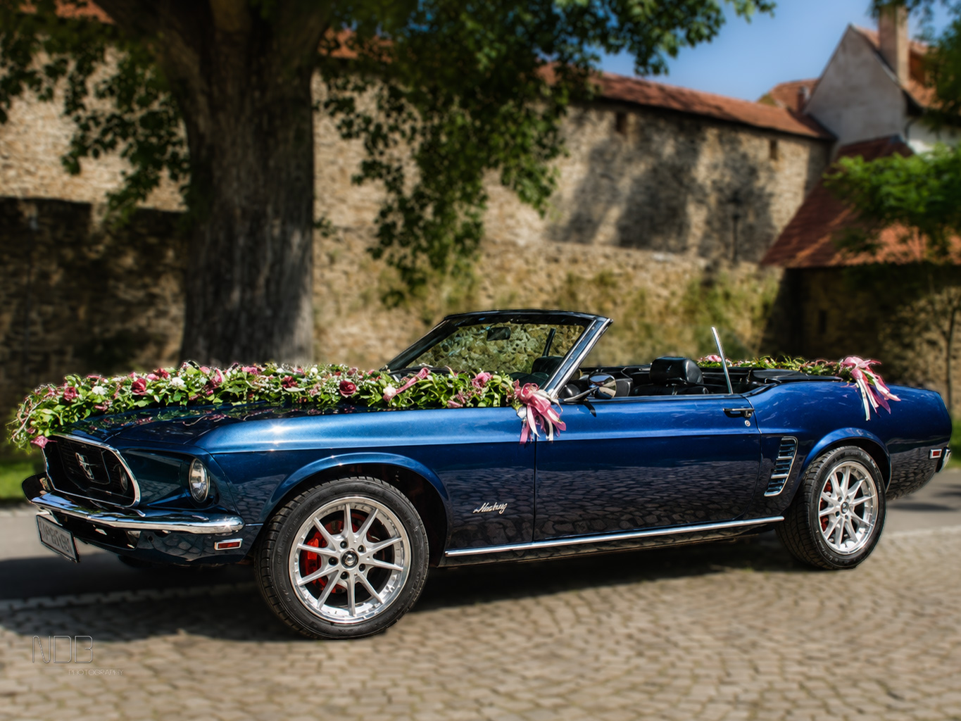 Mit Blumen geschmücktes 1969 Ford Mustang Cabrio in der Seitenansicht vor einer Steinmauer